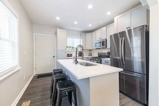 kitchen featuring a breakfast bar area, decorative backsplash, dark wood-style flooring, appliances with stainless steel finishes, and a sink