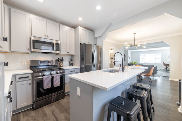 kitchen with a notable chandelier, a breakfast bar, a sink, appliances with stainless steel finishes, and decorative backsplash