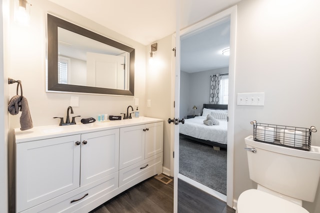 ensuite bathroom with connected bathroom, toilet, double vanity, wood finished floors, and a sink