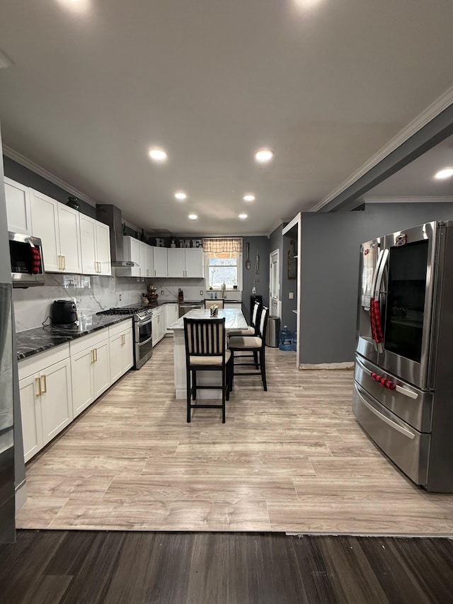 kitchen with light wood finished floors, stainless steel appliances, wall chimney exhaust hood, and ornamental molding