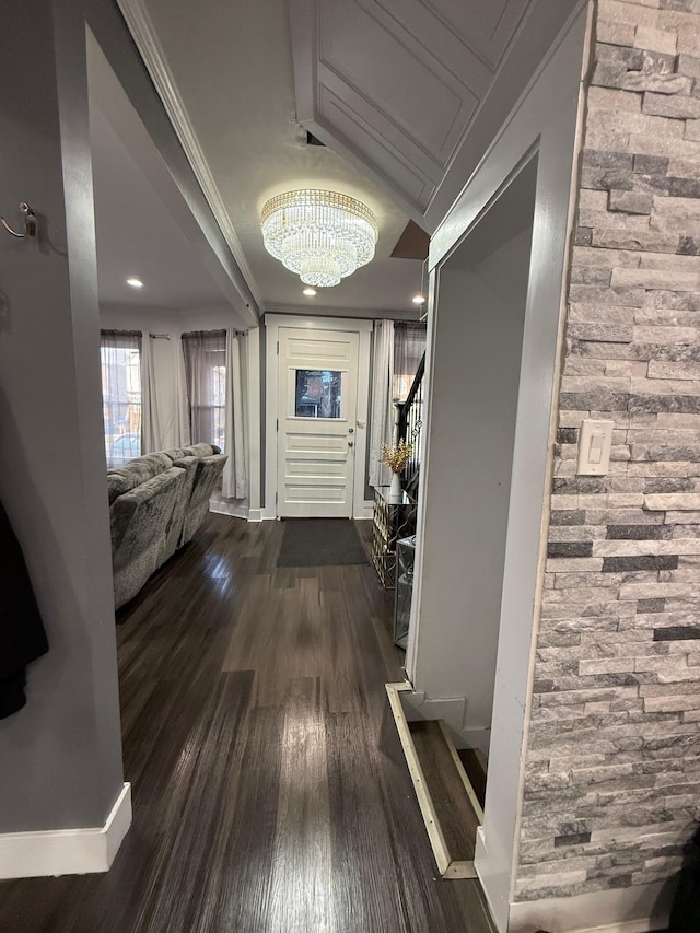 corridor with crown molding, dark wood-type flooring, baseboards, stairs, and a notable chandelier