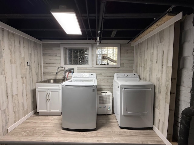 clothes washing area with wooden walls, washing machine and dryer, light wood-style floors, and a sink