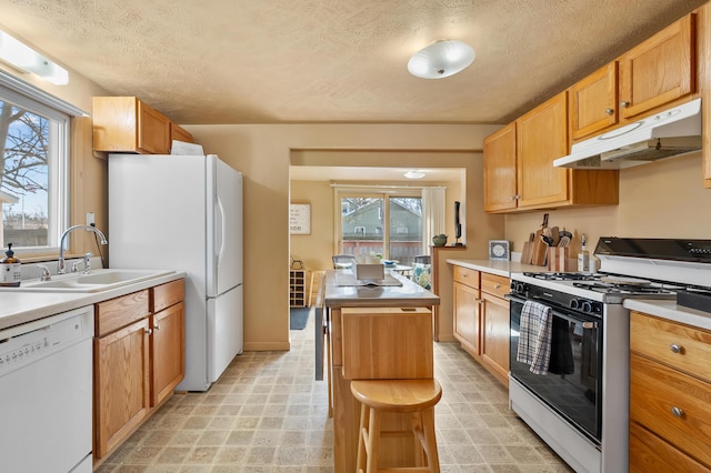 kitchen featuring a kitchen island, under cabinet range hood, light countertops, white appliances, and a sink