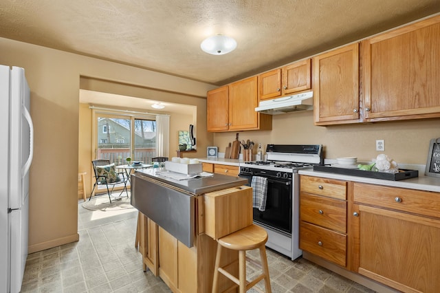 kitchen featuring light floors, a kitchen island, freestanding refrigerator, under cabinet range hood, and gas range