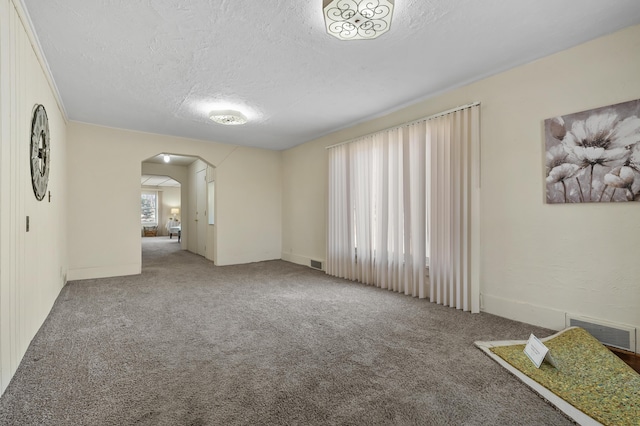 spare room featuring visible vents, arched walkways, a textured ceiling, and carpet flooring