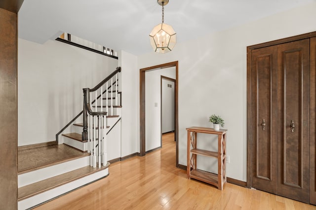 foyer entrance with light wood-type flooring, baseboards, a notable chandelier, and stairs