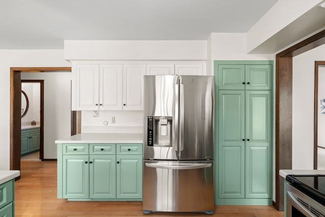 kitchen with light wood-type flooring, stainless steel fridge, white cabinets, light countertops, and green cabinetry