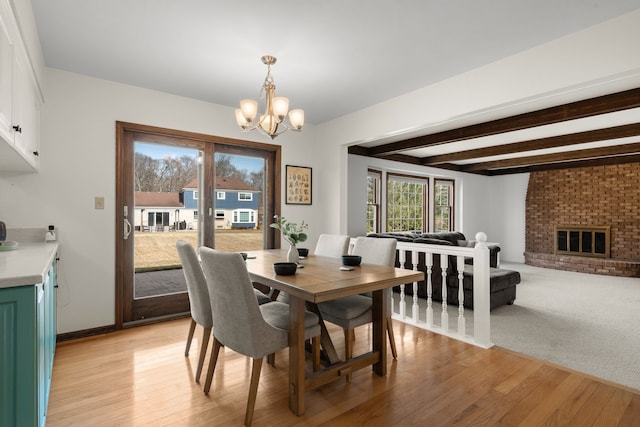 dining space with beam ceiling, a notable chandelier, a fireplace, and light wood-type flooring