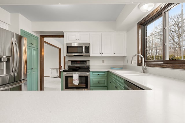 kitchen with green cabinetry, stainless steel appliances, white cabinetry, and a sink