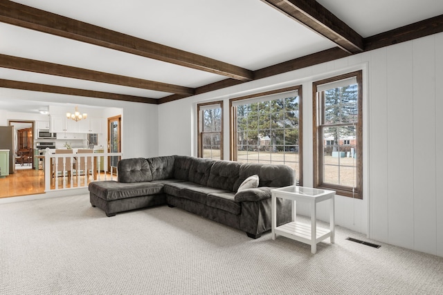 living area with visible vents, light colored carpet, beamed ceiling, and a chandelier