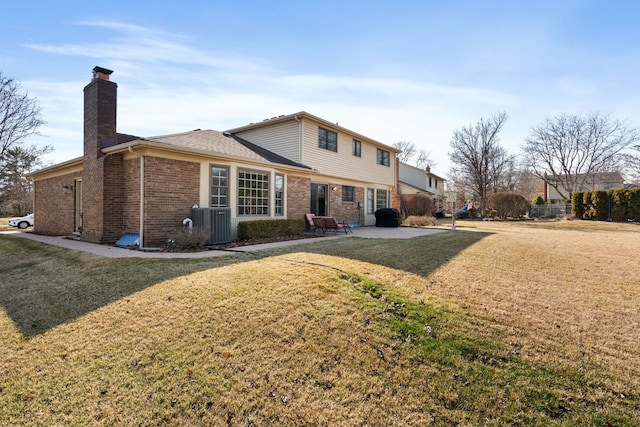 back of property featuring brick siding, a chimney, a lawn, and a patio area