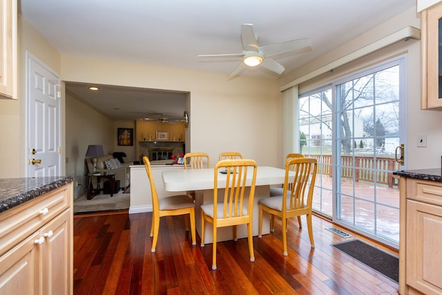 dining area with ceiling fan, dark wood-style floors, visible vents, and a glass covered fireplace