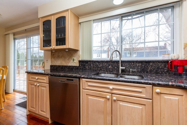 kitchen with light brown cabinetry, a sink, glass insert cabinets, dishwasher, and tasteful backsplash