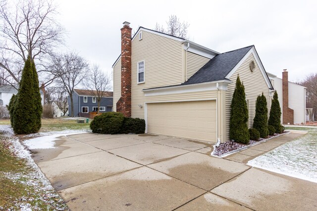 view of side of property with an attached garage, concrete driveway, a chimney, and roof with shingles