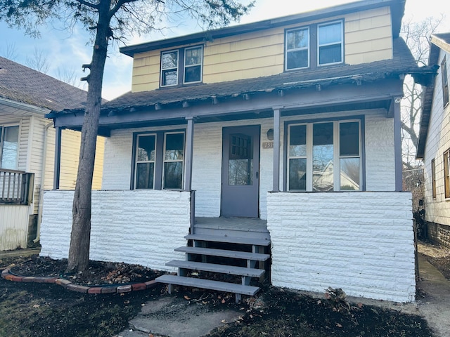 bungalow-style home with covered porch, stone siding, and a shingled roof