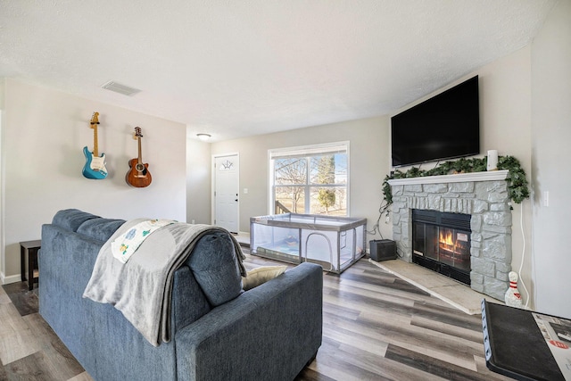 living area with visible vents, a fireplace, a textured ceiling, and wood finished floors