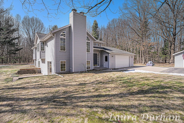 view of property exterior with an attached garage, a chimney, driveway, and a lawn