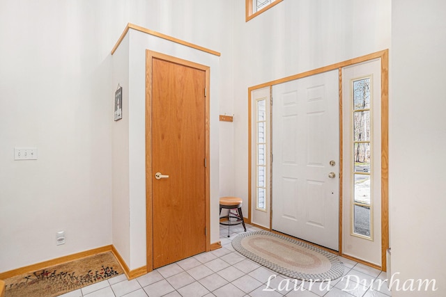 foyer featuring light tile patterned flooring, a high ceiling, and baseboards