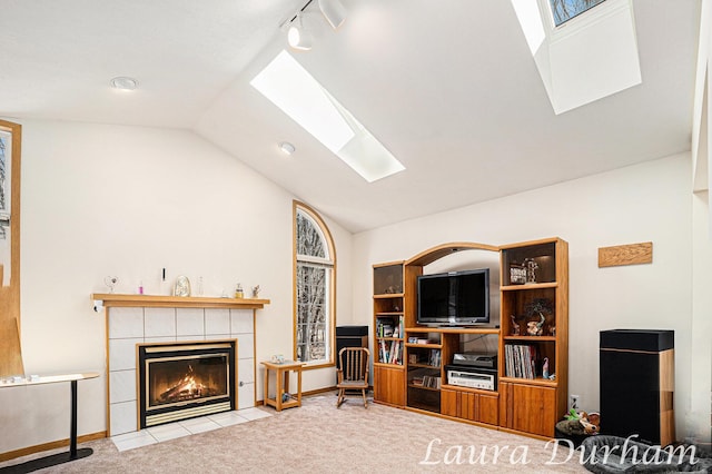 carpeted living area with track lighting, vaulted ceiling with skylight, a fireplace, and baseboards