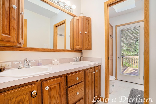 bathroom with double vanity, a skylight, toilet, and a sink