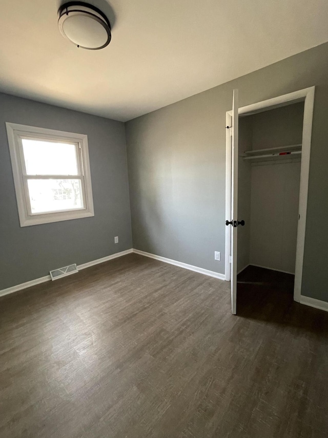 unfurnished bedroom featuring visible vents, baseboards, a closet, and dark wood finished floors