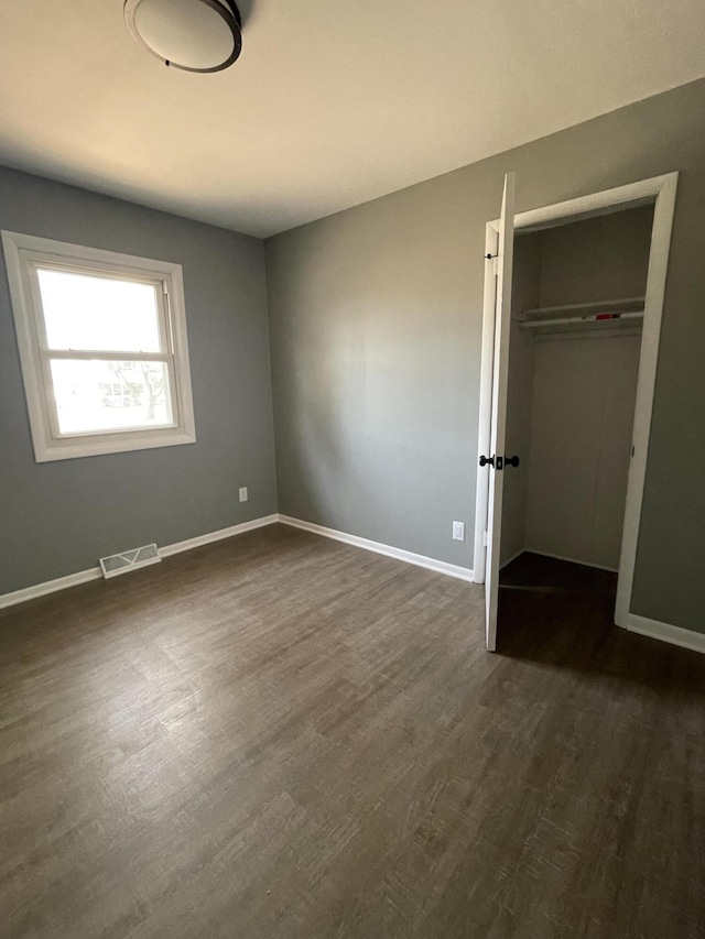 unfurnished bedroom with a closet, visible vents, baseboards, and dark wood-style flooring