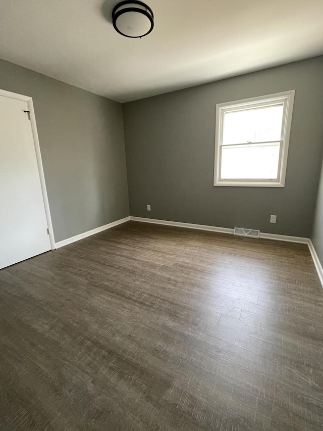 empty room featuring baseboards, visible vents, and dark wood-style flooring