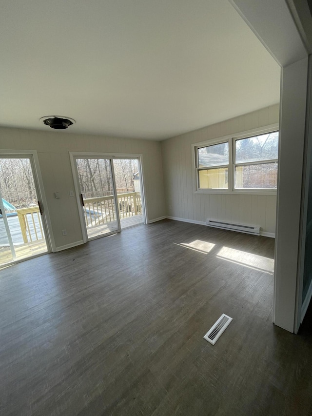 spare room with dark wood-style floors, visible vents, a healthy amount of sunlight, and a baseboard heating unit