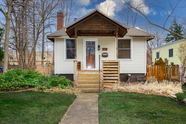 bungalow-style home featuring a front lawn, fence, roof with shingles, and a chimney