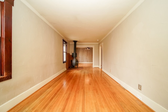 empty room featuring baseboards, light wood finished floors, a wood stove, and crown molding