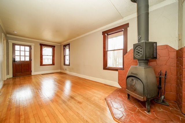 interior space with baseboards, visible vents, a wood stove, crown molding, and light wood-type flooring