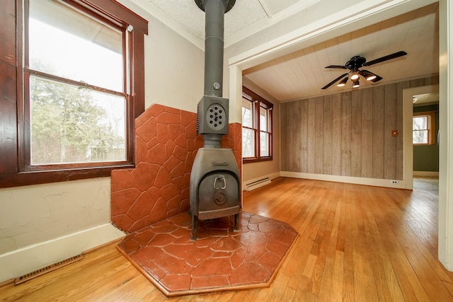 living area with wood-type flooring, baseboard heating, ornamental molding, and a wood stove