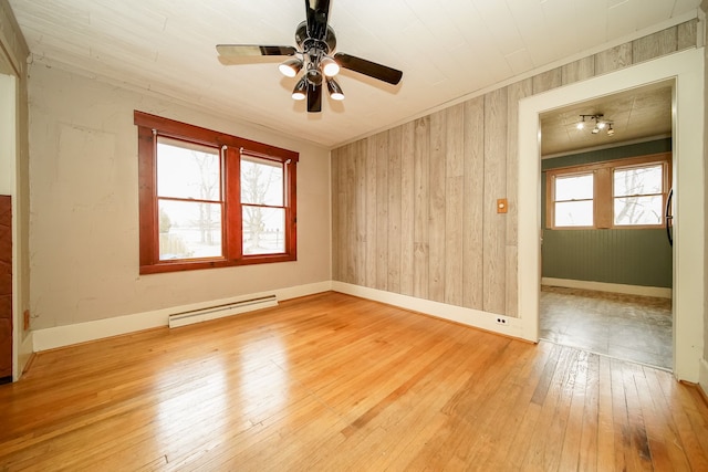 empty room featuring hardwood / wood-style floors, baseboards, ornamental molding, wood walls, and baseboard heating