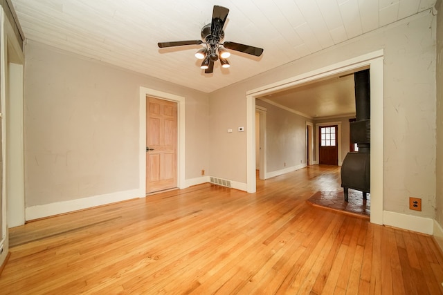 spare room with a ceiling fan, visible vents, baseboards, a wood stove, and light wood-style floors