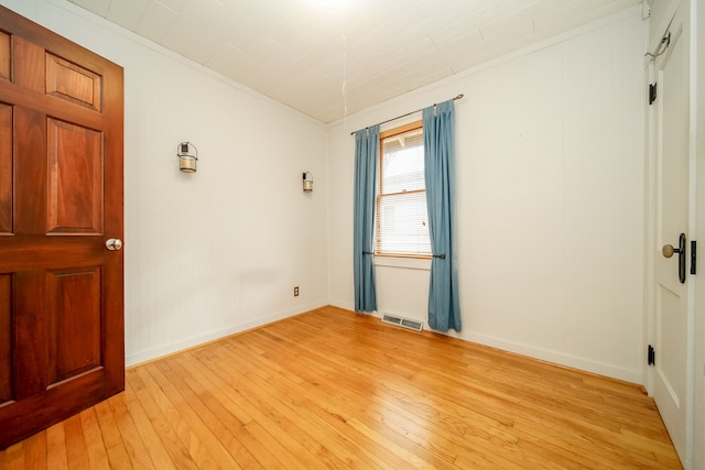 empty room featuring crown molding, light wood-style floors, visible vents, and baseboards