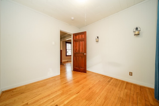 empty room with baseboards, light wood-style flooring, and crown molding