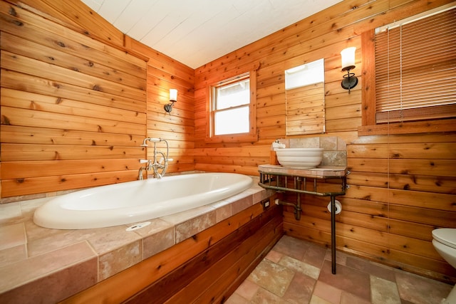 full bath with toilet, stone finish floor, and a bath