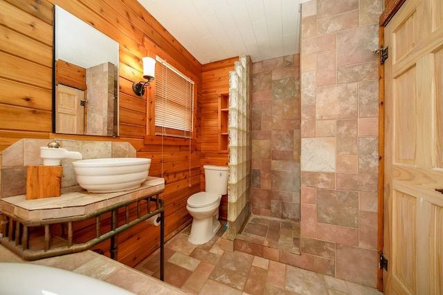 bathroom featuring stone finish flooring, walk in shower, wood walls, toilet, and vanity