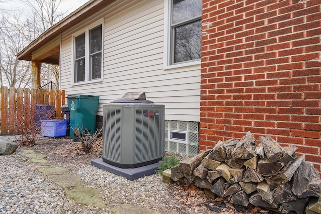 exterior details featuring cooling unit, brick siding, and fence