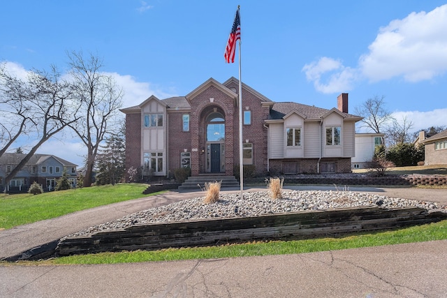 view of front facade featuring brick siding, a chimney, and a front lawn