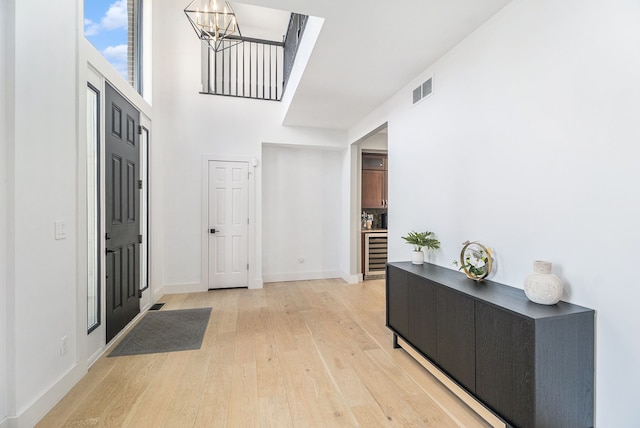 entrance foyer with visible vents, baseboards, wine cooler, a notable chandelier, and light wood-type flooring