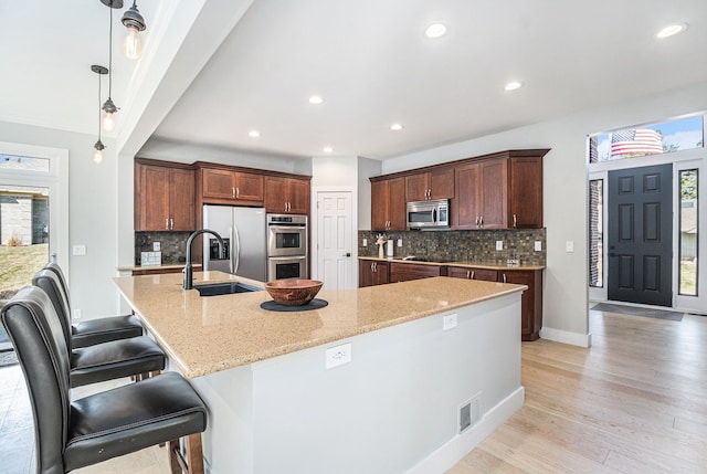 kitchen with light stone counters, a sink, a large island, light wood-style floors, and appliances with stainless steel finishes