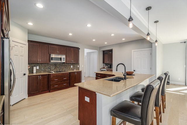 kitchen with light wood finished floors, a sink, stainless steel appliances, a kitchen bar, and backsplash