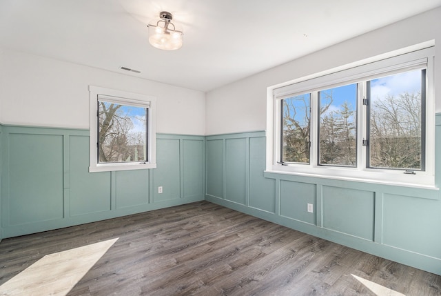 spare room featuring a wealth of natural light, a decorative wall, visible vents, and wood finished floors