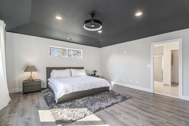 bedroom with recessed lighting, baseboards, wood finished floors, and brick wall