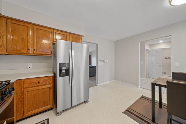 kitchen featuring brown cabinets, stainless steel appliances, light countertops, baseboards, and light floors