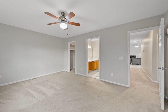 unfurnished bedroom featuring a spacious closet, baseboards, light carpet, ensuite bath, and a ceiling fan