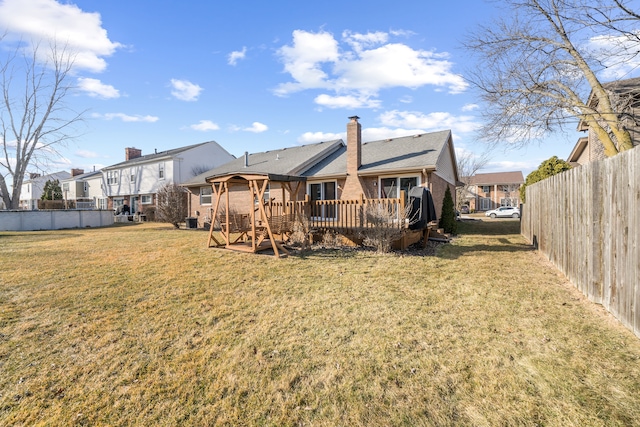 rear view of property with brick siding, fence, a lawn, a chimney, and a deck