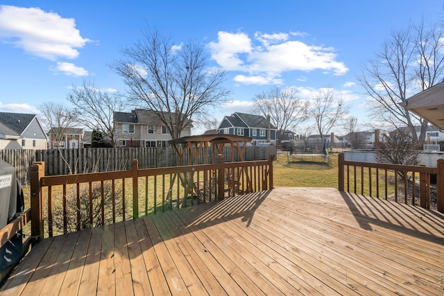 wooden terrace featuring a residential view, a trampoline, a lawn, and fence