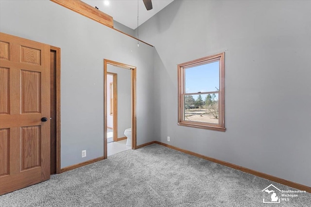 unfurnished bedroom featuring a high ceiling, ensuite bathroom, baseboards, and carpet floors